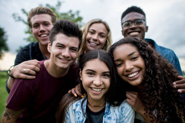 youth photo A multi-ethnic group of teenagers are outdoors on a cloudy day. They are wearing casual clothing. They are smiling while taking a selfie together.
